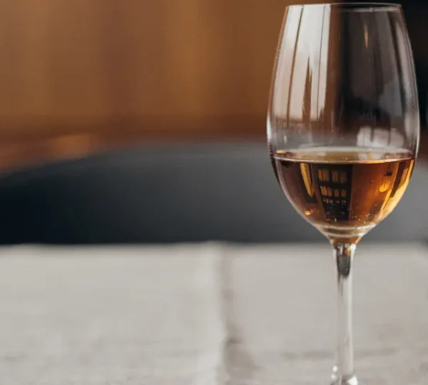 A white wine glass holding a small pour of aged amber rum on a fine-dining table, lit like an editorial magazine photo with ample negative space.