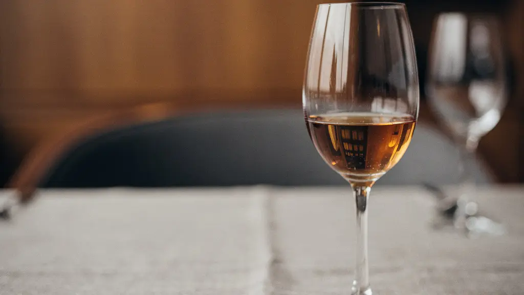 A white wine glass holding a small pour of aged amber rum on a fine-dining table, lit like an editorial magazine photo with ample negative space.
