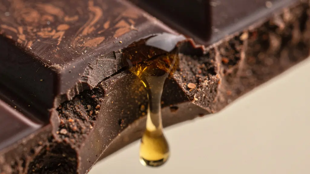 Extreme close-up of dark chocolate surface showing crystalline texture and melting edge with warm amber liquid nearby