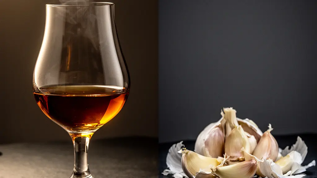 A tulip-shaped cognac glass with warm amber liquid on one side and crushed garlic cloves on the other, separated by dramatic lighting