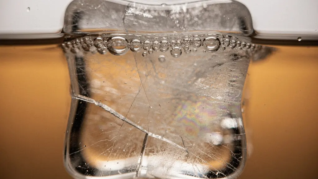 Extreme close-up macro photograph of an ice cube surface immersed in a spirit, showing the thin boundary layer of meltwater forming between ice and liquid