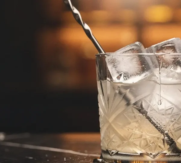 A crystal mixing glass filled with ice and a clear spirit, with condensation droplets catching soft light, illustrating the science of cocktail dilution