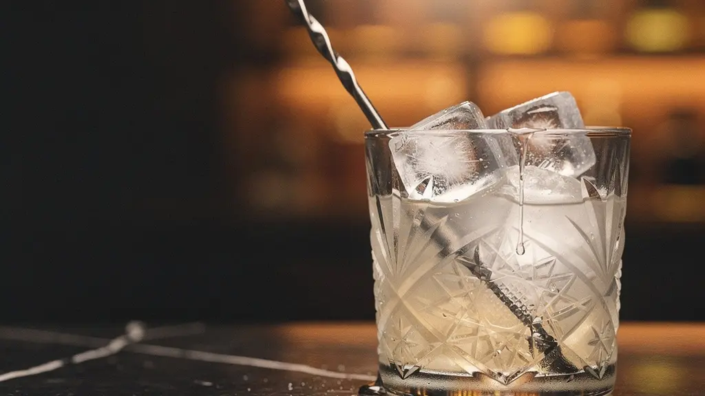 A crystal mixing glass filled with ice and a clear spirit, with condensation droplets catching soft light, illustrating the science of cocktail dilution
