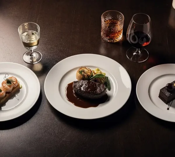 Elegant three-course dinner table set with spirit glasses and food pairings in warm lighting